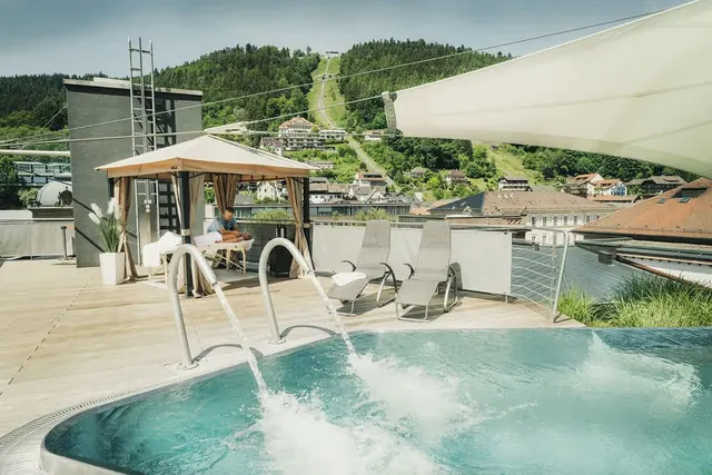 Outdoor rooftop hot spring pool with water jets, lounge chairs, and mountain view overlooking the town of Bad Wildbad at Palais Thermal Ger.