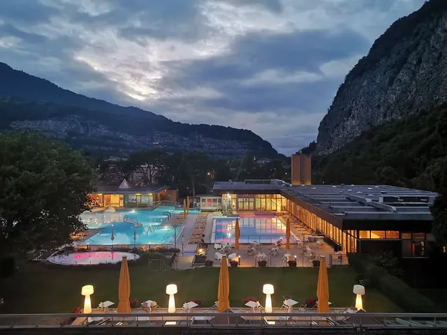 Evening view of illuminated outdoor pools and patio seating at Les Bains de Lavey with mountain backdrop near Saint-Maurice Switzerland.