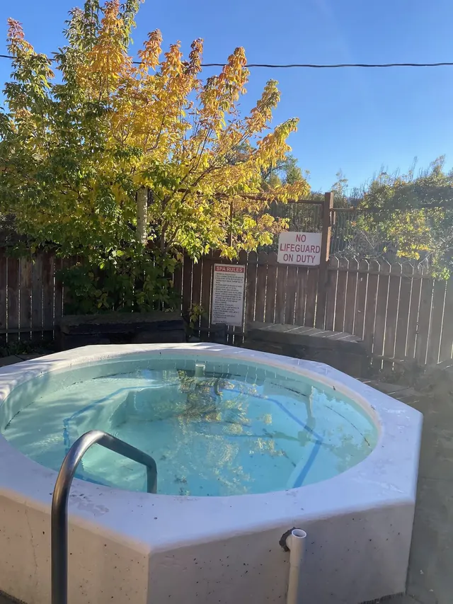 Steaming round outdoor hot tub surrounded by wooden fence and autumn foliage at Symes Hot Springs in Hot Springs Montana.