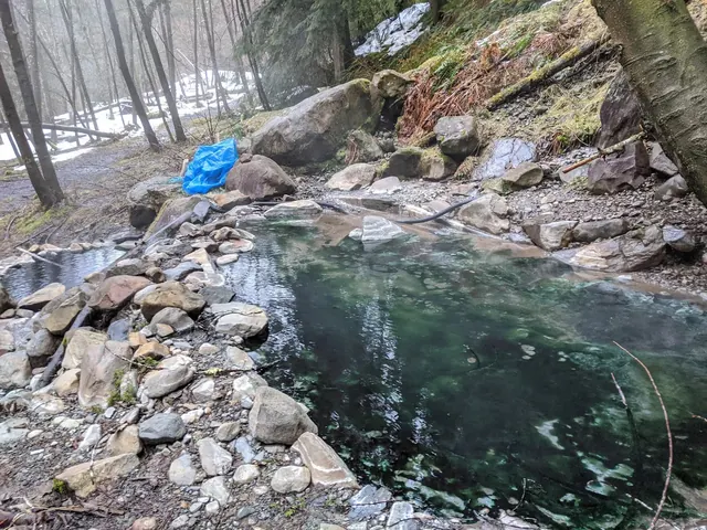 Steam rising from a rock-lined hot spring water pool by a forest trail at Olympic Hot Springs near Port Angeles Washington.
