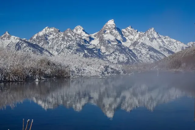Calm natural hot spring pond at Kelly Hot Springs reflecting snow-capped mountain peaks near Kelly, Wyoming.