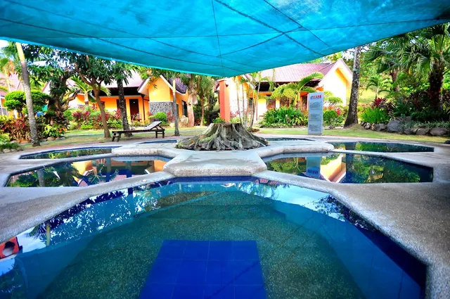 Outdoor hot spring pool at 88 Hot Spring Resort with shade cloth cover surrounded by tropical plants and cottages in Calamba City Philippin.
