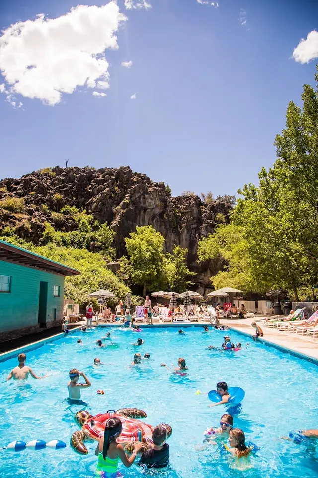Outdoor pool at Veyo Pool Hot Springs near St. George Utah filled with people swimming on a sunny day under blue sky.