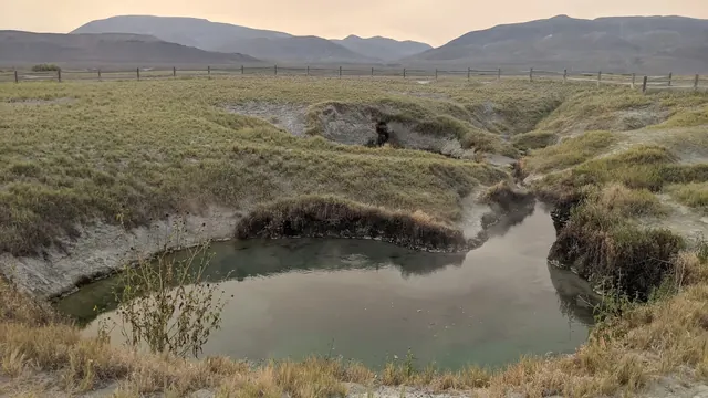 Steam gently rising from the calm waters of Double Hot Springs amid grassy terrain and fenced fields near Gerlach, Nevada