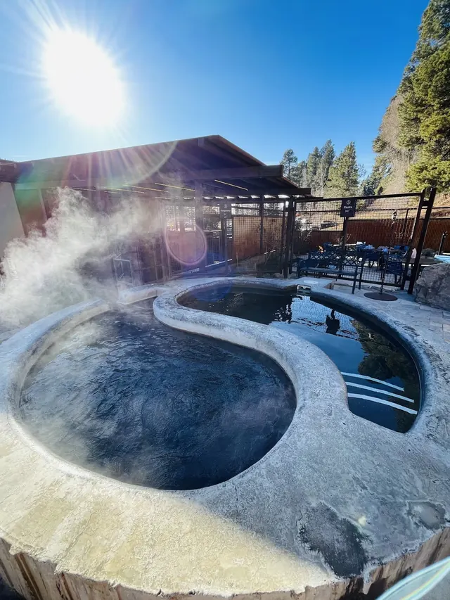 Steaming yin-yang shaped dual soaking pools under bright sun at Durango Hot Springs in Durango, Colorado, United States.