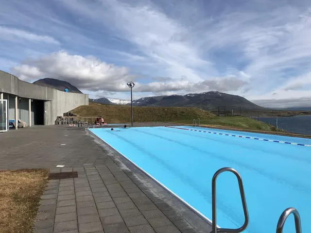 Wide view of Hofsos Swimming Pool outdoor pool with swimmers, surrounded by paved walkway and mountainous landscape near Hofsos Iceland.