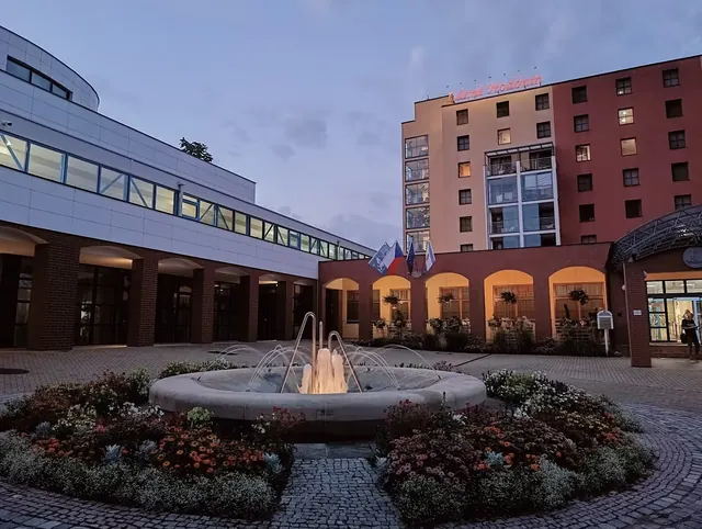 Outdoor stone fountain surrounded by flower beds in a courtyard of Lazne Hodonin spa during early evening in Hodonin, Czechia.