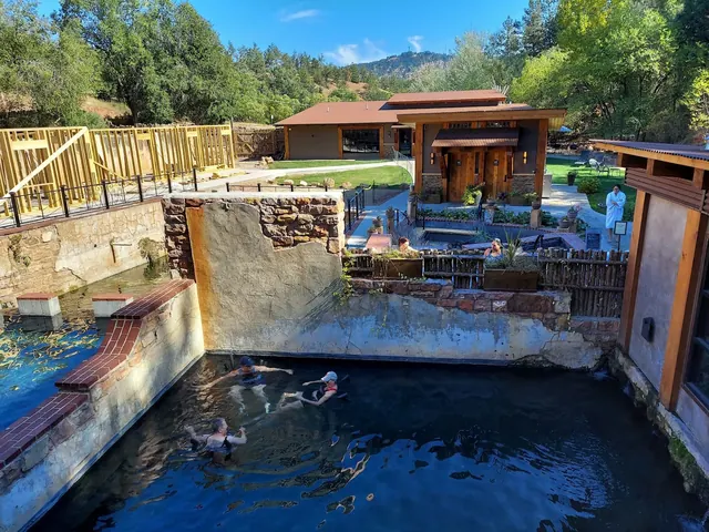 Several people soaking in a dark water hot spring pool at Moccasin Springs Natural Mineral Spa in Hot Springs South Dakota with spa buildin.