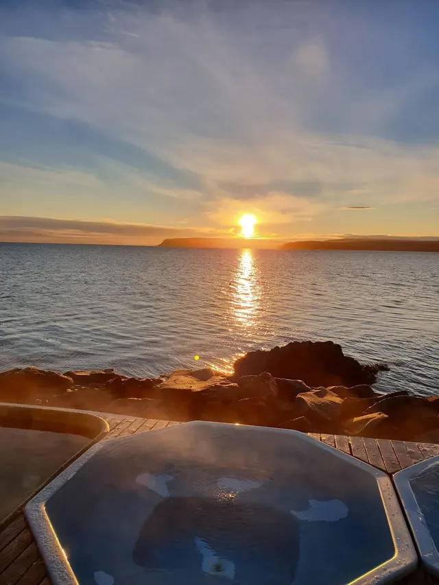 Steaming octagonal hot spring pool at sunset with golden sun reflecting over the ocean near Drangsnes, Iceland.