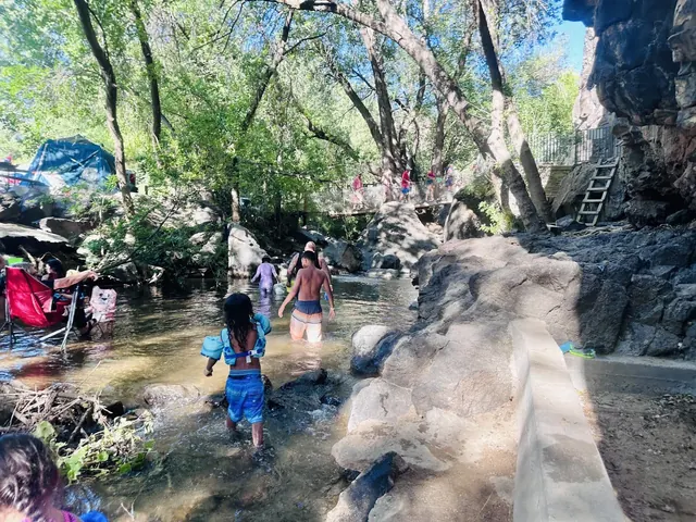 Natural hot spring pool surrounded by rocks and trees with people wading in the water at Veyo Pool Hot Springs in Utah.