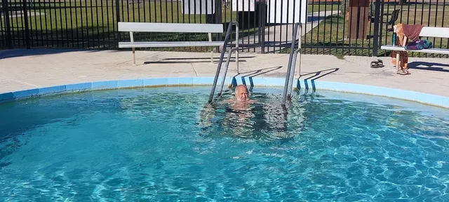 Man soaking in the circular hot spring pool with metal ladder and bench seating at Walgett Artesian Bore Baths, Australia on a sunny day.