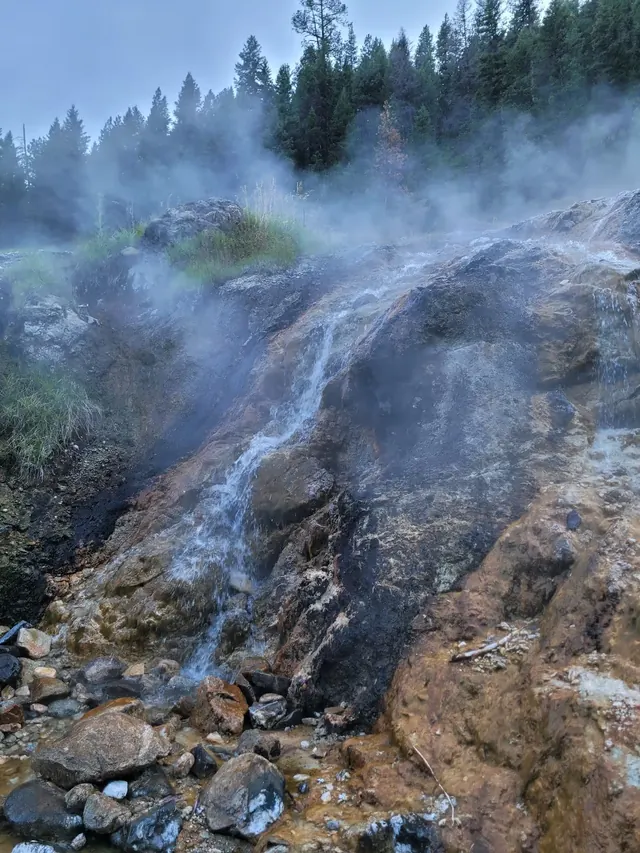 Rocky hot spring waterfall with thick steam rising surrounded by forest at Bonneville Hot Springs near Lowman, Idaho, United States