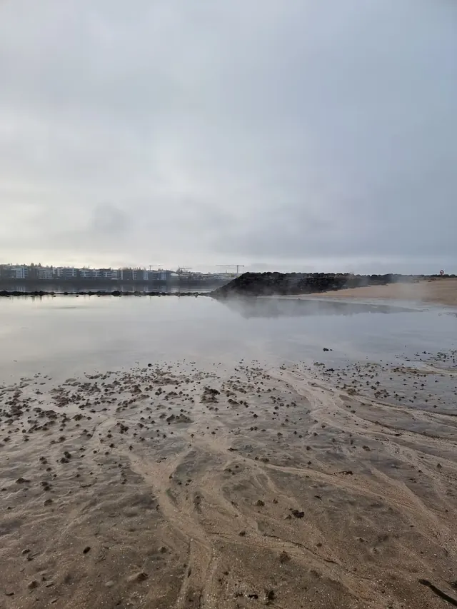 Steamy shoreline view at Nautholsvik geothermal beach with calm water near Reykjavik Iceland.