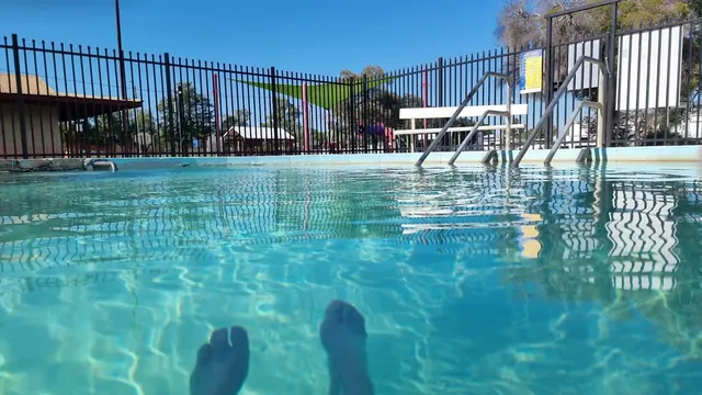 View from inside the hot spring pool showing feet and rippling water with metal stairs and fence in the background at Walgett Artesian Bore.