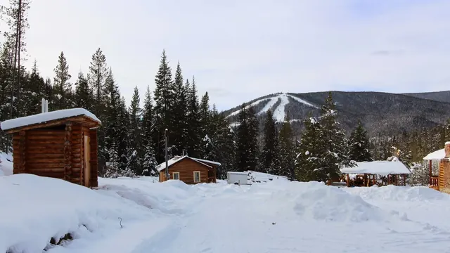 Rustic wooden lodge with a large sign for Elkhorn Hot Springs nestled in a shaded forest area near Polaris, Montana.