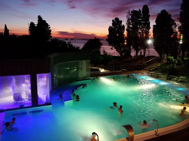 Evening scene of La Parenthese Obalia outdoor pool glowing under lights with a purple sunset sky along Sete shore.