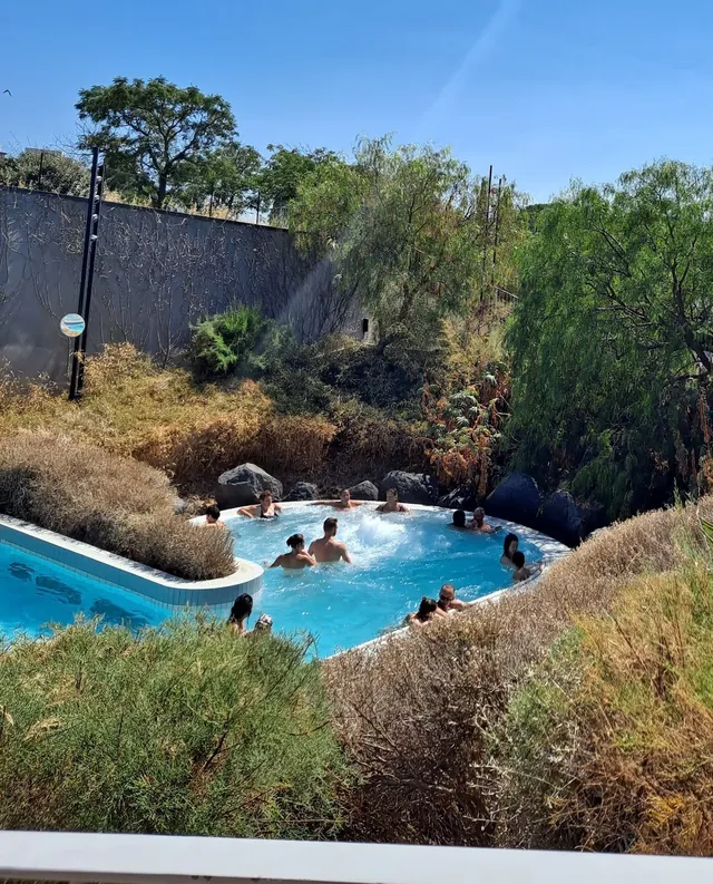 Naturalistic outdoor pool at La Parenthese Obalia surrounded by green trees and shrubs with people enjoying the warm water.