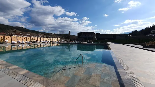 Daytime view of a spacious outdoor mineral pool with sun chairs and umbrellas under a clear blue sky near Grand Hotel Therme in Banya, Bulg.