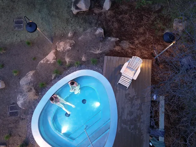 Aerial view showing two people soaking in a heart-shaped pool at The Springs with lounge chair and garden lights.