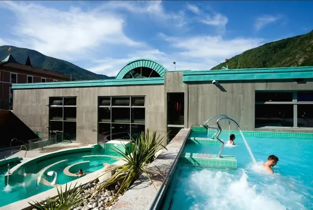 Outdoor terraces of Les Bains du Couloubret show multiple pools with water jets and visitors surrounded by hills outside Ax-les-Thermes Fra.