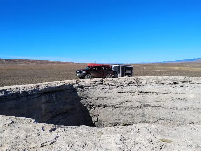 Pickup truck and trailer parked on rim of Diana’s Punch Bowl hot spring crater with visible water, located in Nevada desert near Round Mountain