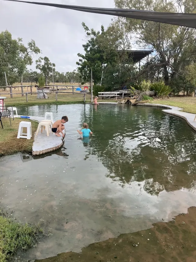 Children play in a greenish water pool with shaded cover at Lara Wetlands thermal pool near Barcaldine area Queensland Australia.