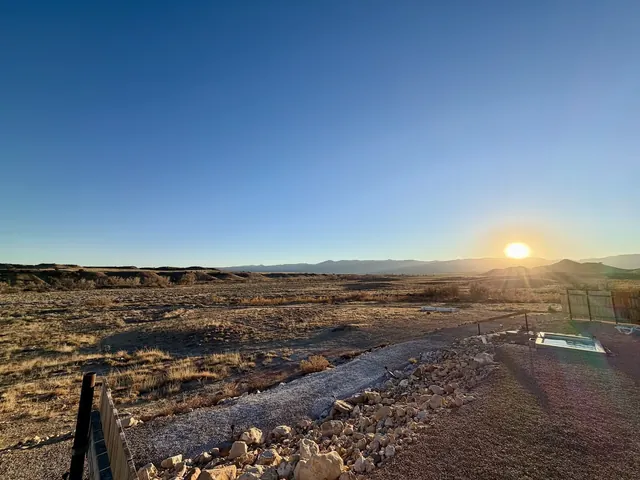 Wide view of Desert Reef Hot Springs with clear blue water pool at sunset near Florence, Colorado, showing arid terrain and distant mountains.