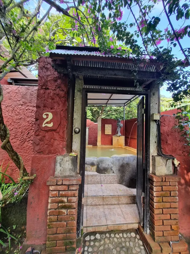 Entrance to a private hot spring pool with red brick and plaster walls covered by purple flowering vines in Bali.