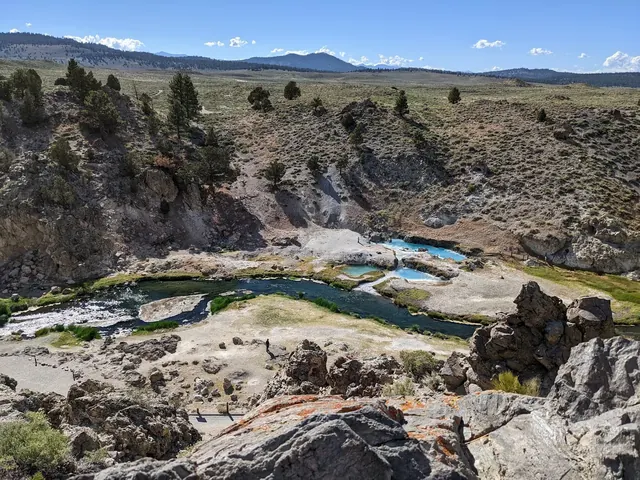 A rocky overlook showing multiple blue hot spring pools by a river and sparse vegetation at Hot Creek Geologic Site in california.