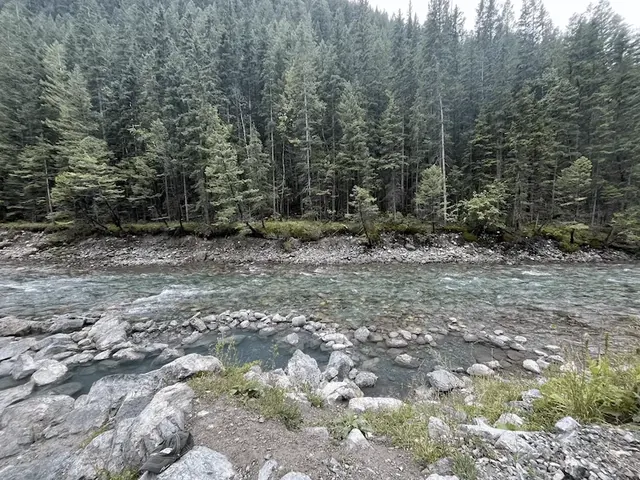 Rock lined natural hot spring pools beside the lussier river and with forest in the background at lussier hot springs in canada