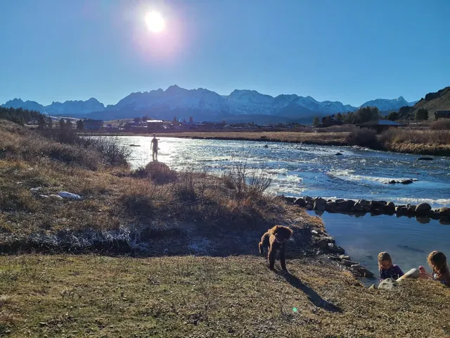 Outdoor natural hot spring pool by the river with mountains in the background at Mountain Village Resort Hot Springs near Stanley, Idaho