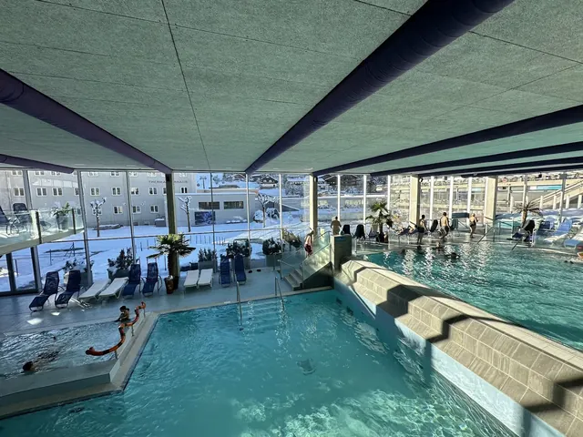 Indoor pool area at Felsentherme Bad Gastein with people soaking, glass walls showing winter snow, and blue water features in Bad Gastein.