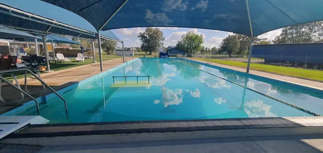Large rectangular soaking pool at Boomi Artesian Spa Pools with clear blue water and shade structures along the poolside.