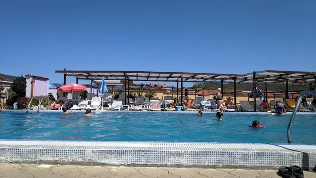 Low angle view of large outdoor pool with light blue tiles and people swimming on a sunny day in Velingrad.