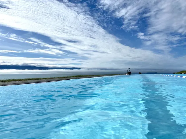 Clear bright blue water in Hofsos Swimming Pool outdoor pool with swimmers at the far end and low fog over water near Hofsos Iceland.