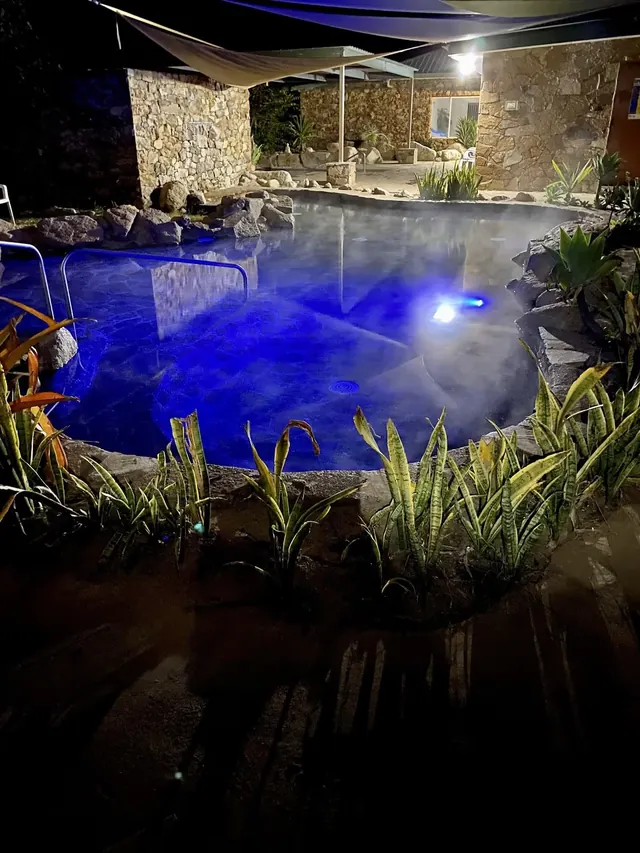 Night view of a steamy hot spring pool lit with blue lights and surrounded by stone walls at Innot Hot Springs in Queensland Australia.