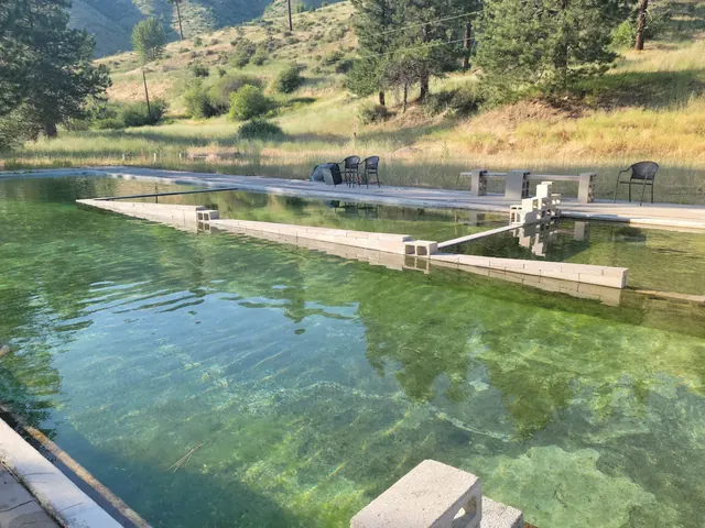 Clear water of Haven Hot Springs outdoor pool in Lowman, Idaho, surrounded by green hills and a few chairs along the concrete edge.