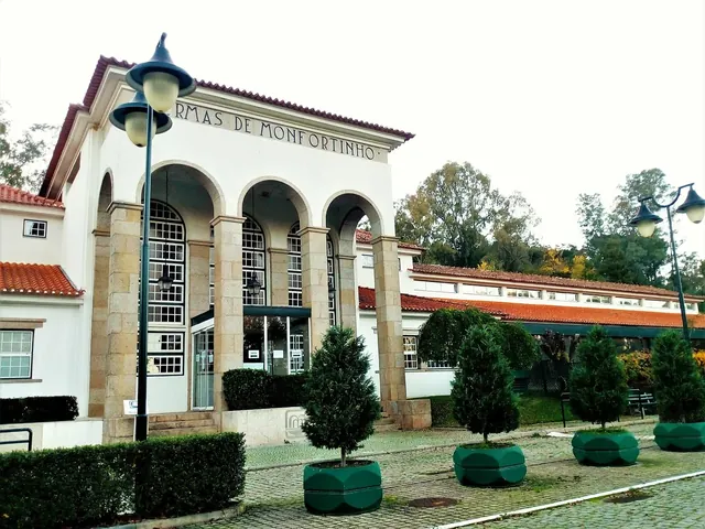 Front exterior of Termas de Monfortinho building with tall stone pillars and arched windows under a cloudy sky in Monfortinho Portugal.