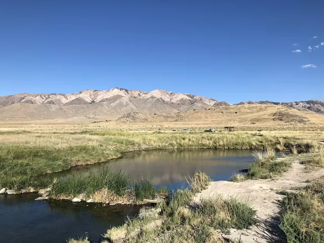 Calm natural pool surrounded by grassy banks with rugged mountains in the background at Horseshoe Springs near Dugway Utah.