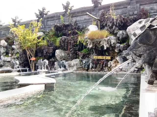 Hot spring pool with natural volcanic rocks and water spouting from stone sculptures at Batur Natural Hot Spring Bali.