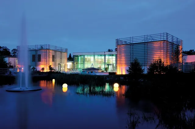 Therme Bad Steben outdoor pool at dusk with illuminated modern buildings reflecting in a calm water pond in Bad Steben germany.