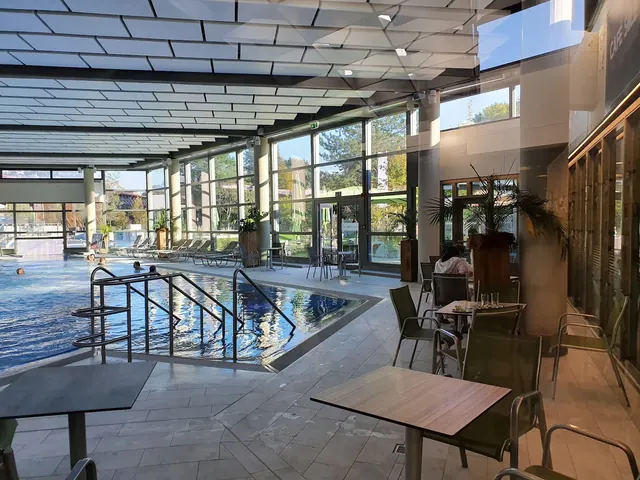 Indoor spa pool with people soaking and tables with chairs near large windows providing natural light at Borde Therme Bad Sassendorf.