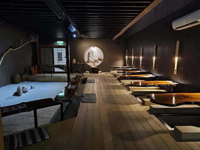 Interior of Japanese Bath House seating area with wooden tables over water foot baths, soft lighting, zen garden, and bamboo wall lamps in.