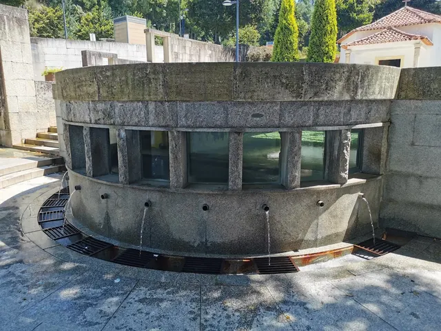 Eight stone spouts pouring water into a semicircular basin at Termas de Luso near Luso, Portugal on a sunny day.
