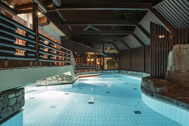 Taunus Therme indoor pool featuring pale blue tiles, a rocky waterfall feature, and warm wood ceiling beams in Bad Homburg.