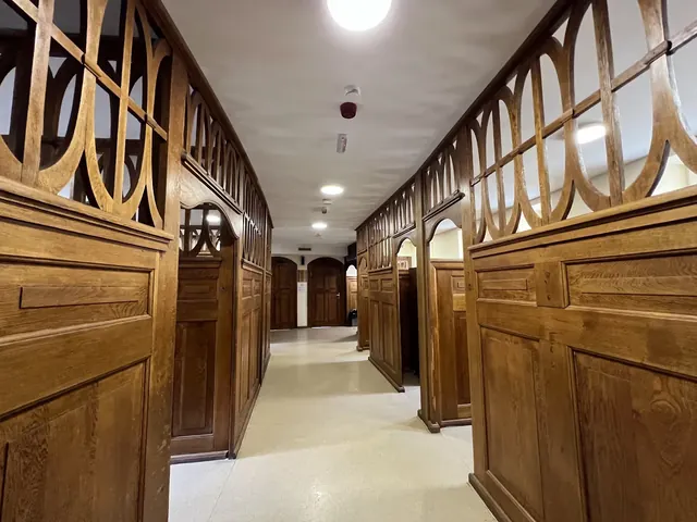 Hallway with wood paneled walls and doors, overhead lights, and cream flooring leading to separate bathing areas at the hot springs in Bank.