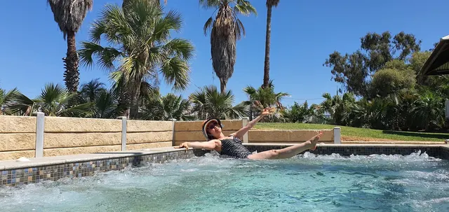 Woman wearing a sunhat enjoys the jets in a rectangular jacuzzi pool surrounded by palm trees at Blackall Aquatic Centre.