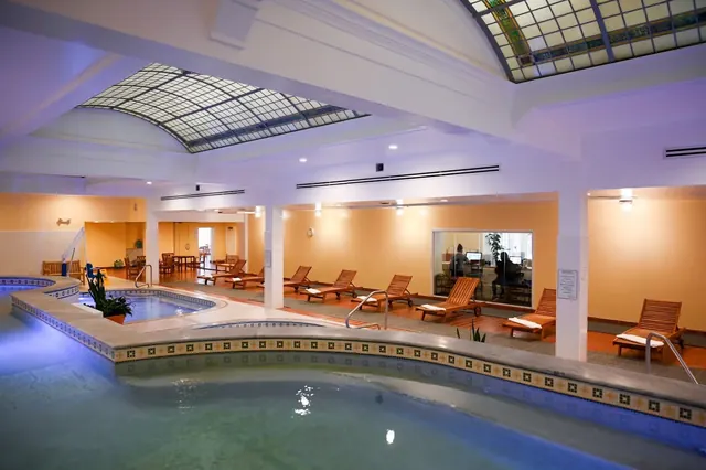 Indoor mineral hot spring pools at Quapaw Baths with mosaic tiled edges and several wooden lounge chairs in Hot Springs, Arkansas.