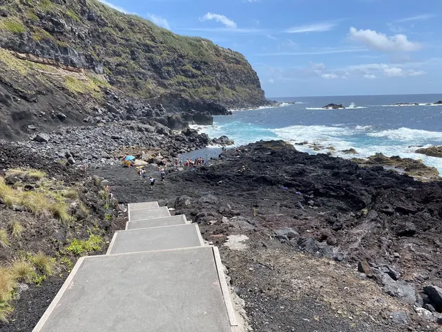 Group of people soaking in a rocky natural pool with waves crashing nearby under cloudy sky at Ponta da Ferraria near Ponta Delgada Portuga.