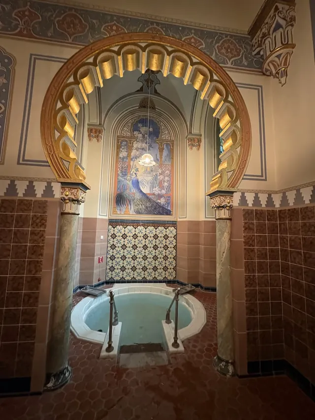 Small indoor hot spring soaking pool at Palais Thermal with decorative tile and a mural of a peacock under an ornate arched ceiling in Bad.